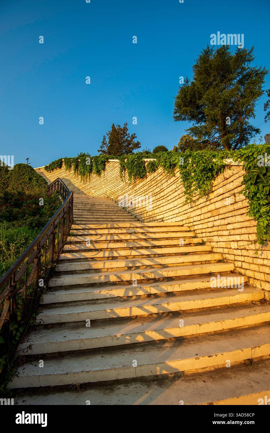 Les marches de pierre de Permet s'élèvent sous une lueur chaude du coucher du soleil, encadrées par des vignes grimpantes et révélant un panorama tranquille sur les collines albanaises Banque D'Images