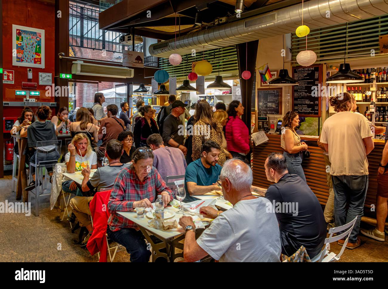 Les gens appréciant la nourriture au Mercato di Mezzo un marché alimentaire couvert animé avec pâtes, viande et fromage, pizza et boissons, plus des sièges de table, Bologne, Italie Banque D'Images