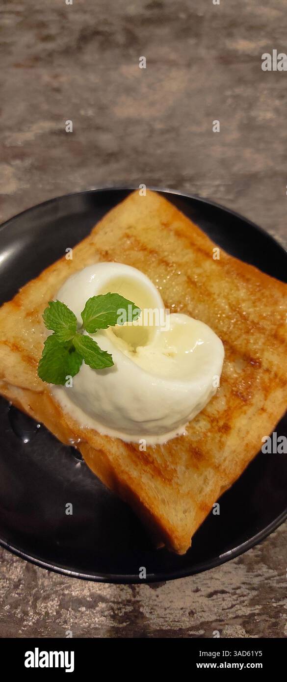 pain grillé simple mais délicieux garni de crème glacée crémeuse à la vanille et d'une feuille de menthe, idéal pour les amateurs de collations et de photographie culinaire Banque D'Images