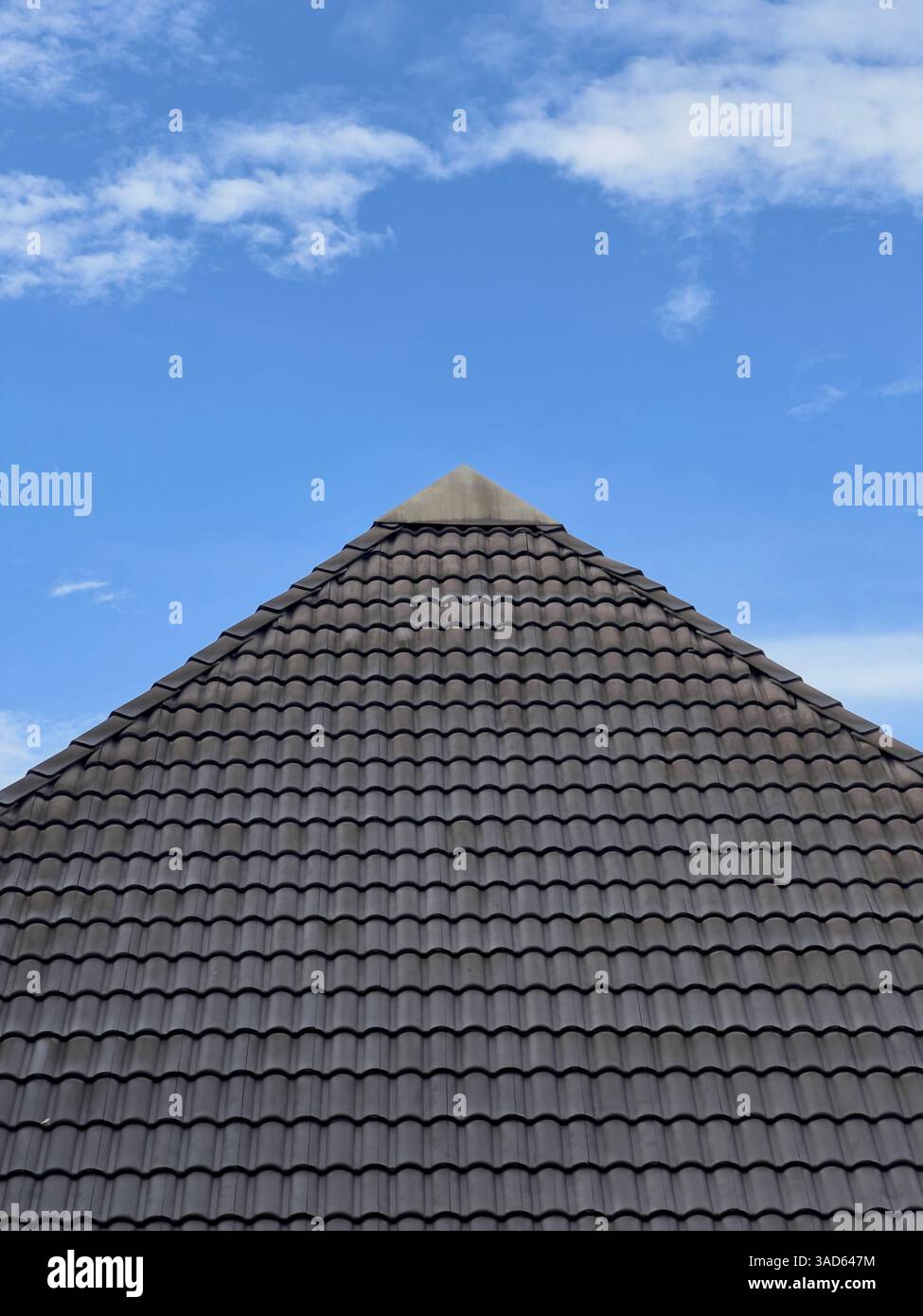 Gros plan d'un toit contemporain orné de tuiles sombres placées contre un ciel bleu vif avec des nuages éparpillés. - Image de stock capturée avec un smartphone