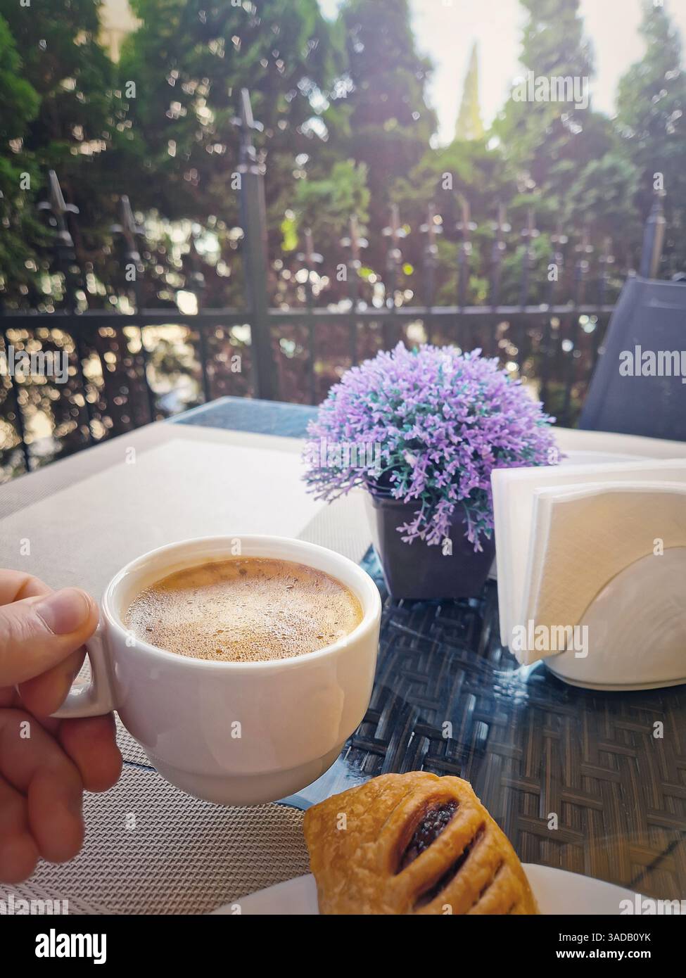 Gros plan main masculine tenant une tasse de café avec de la mousse sur le dessus. Moment tranquille du matin dans le café en profitant de la boisson avec un croissant. Pause petit déjeuner - Image de stock capturée avec un smartphone