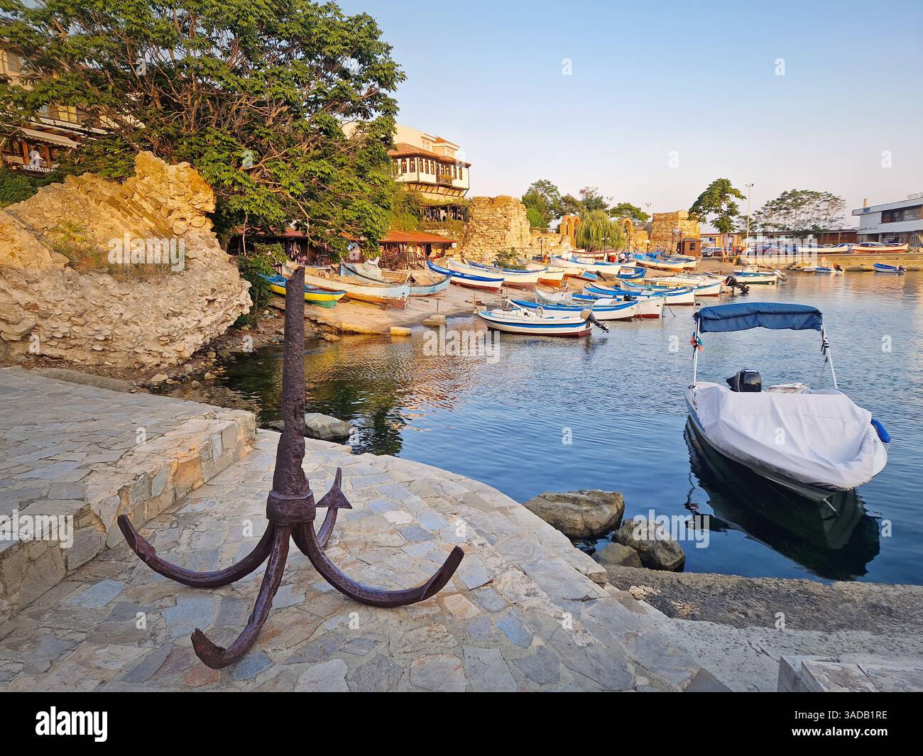 Ancre rouillée au port avec de nombreux bateaux amarrés dans les eaux calmes. Scène de marina sereine dans la lumière chaude du coucher du soleil. Bâtiments traditionnels et anciens - Image de stock capturée avec un smartphone