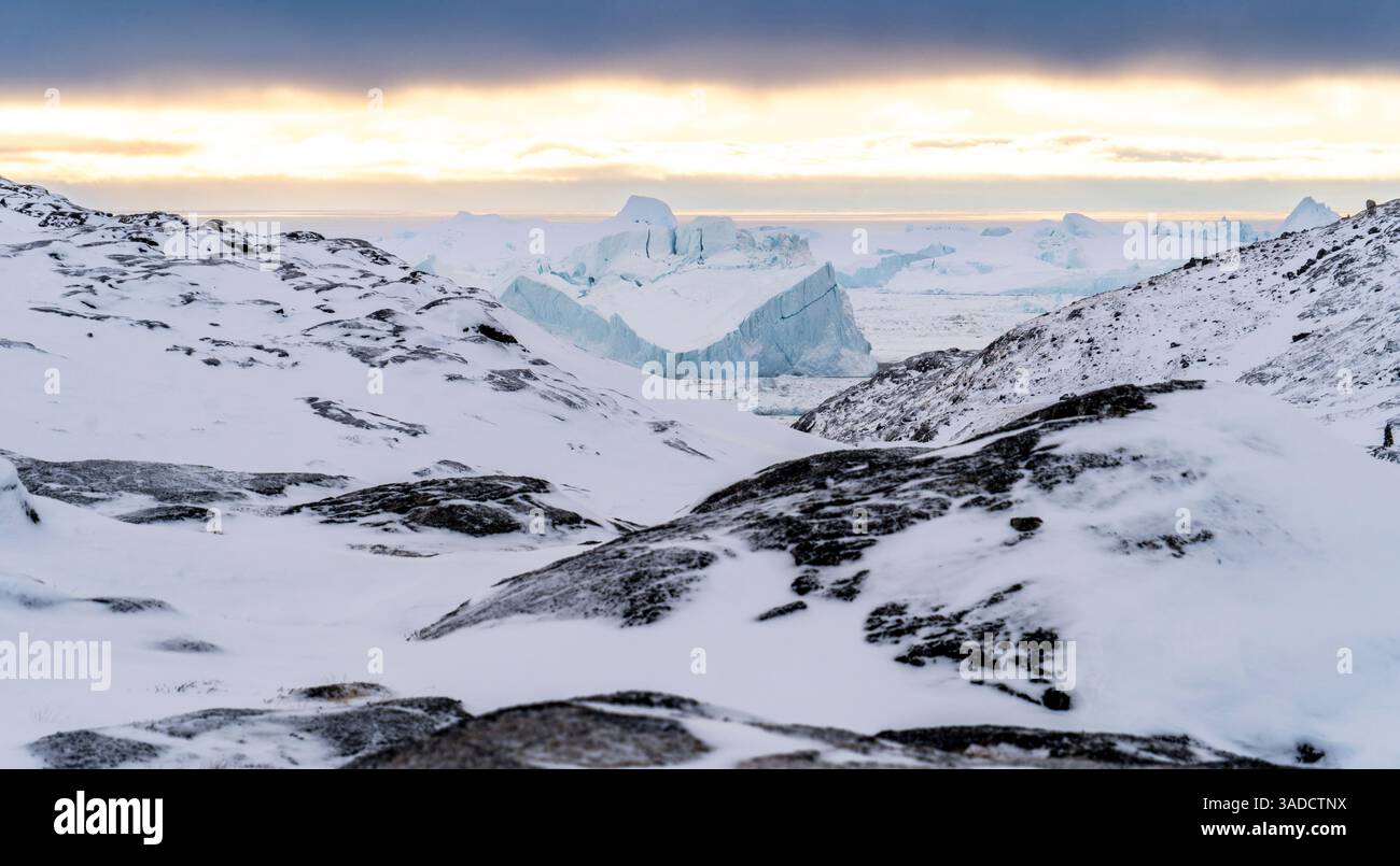 Un paysage hivernal à couper le souffle avec des rochers enneigés au premier plan, menant à une vaste étendue glacée avec d'imposants icebergs au loin. Banque D'Images