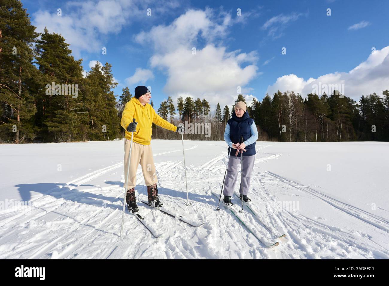 Prenant une courte pause de ski à travers un champ enneigé, couple européen d'âge moyen profite de la journée ensoleillée d'hiver. Banque D'Images