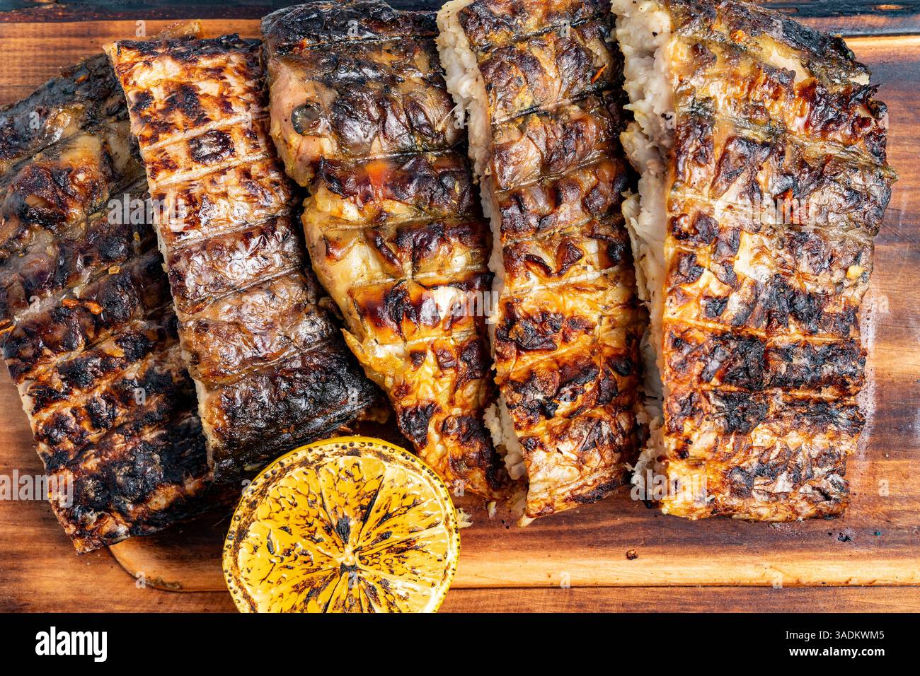 De succulents filets de poisson grillé sont disposés soigneusement sur une planche à découper en bois, accompagnés d'une moitié de citron parfaitement carbonisée qui ajoute du zeste au plat Banque D'Images
