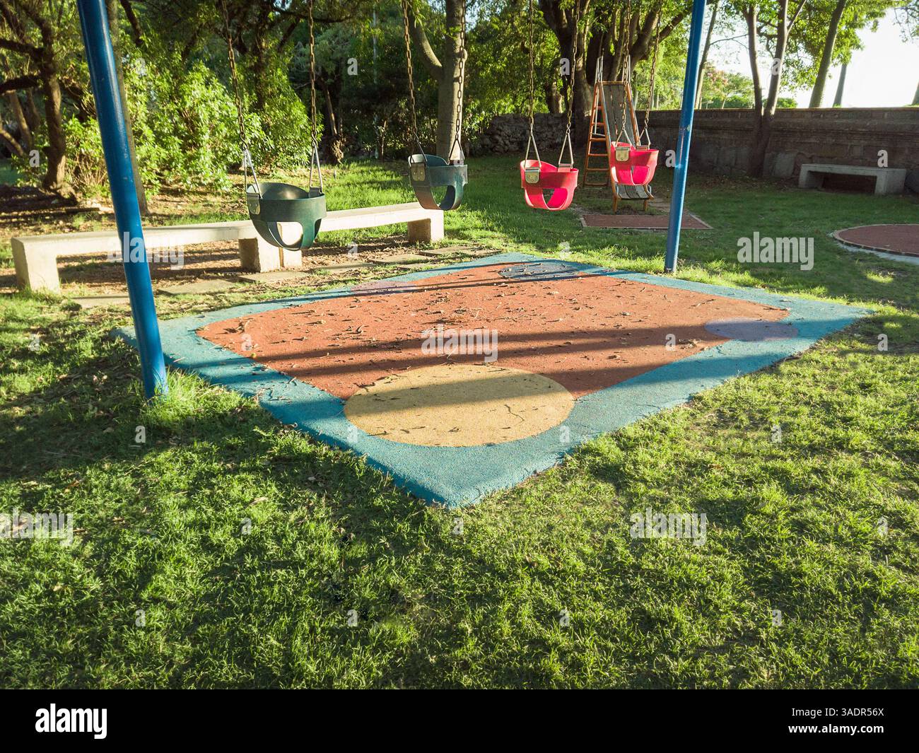 Quatre balançoires pour tout-petits dans un parc calme avec des arbres et la lumière chaude du soleil du soir. Banque D'Images