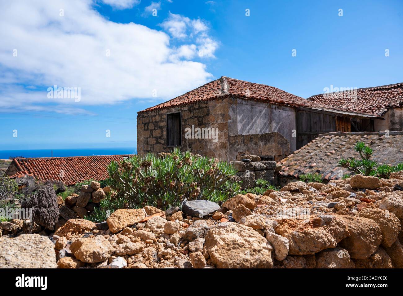 Une petite maison avec un toit rouge se trouve sur une colline rocheuse. La maison est entourée de rochers et il y a un petit buisson qui pousse devant elle. Banque D'Images