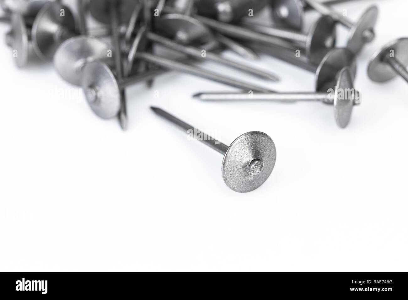Une pile de clous de toiture sur un fond blanc est une quincaillerie métallique essentielle pour les travaux de construction et de réparation. Banque D'Images