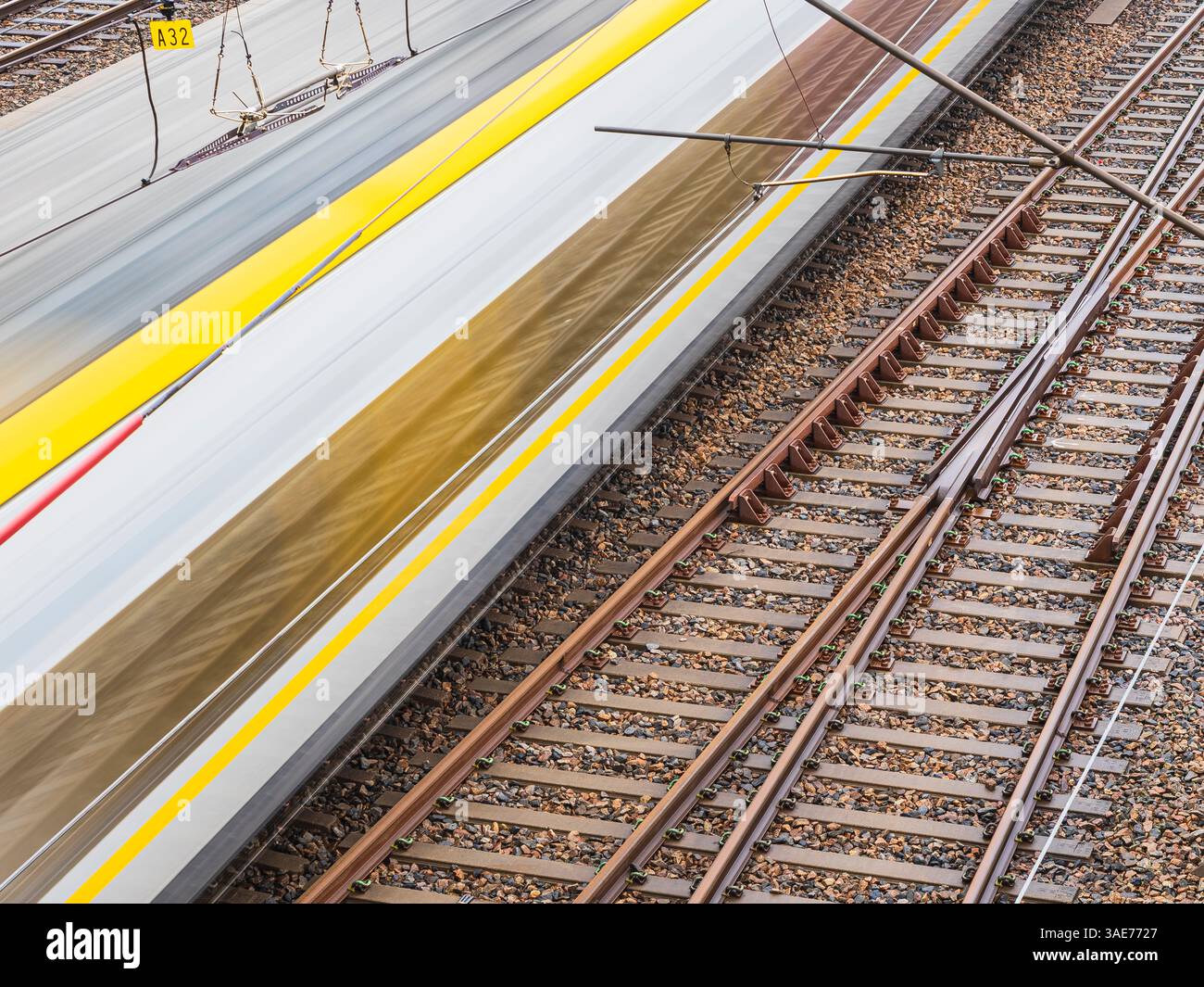 Un train à grande vitesse passe devant les voies ferrées pendant que les passagers attendent et les structures à proximité créent un sentiment de mouvement et d'énergie à une gare très fréquentée Banque D'Images