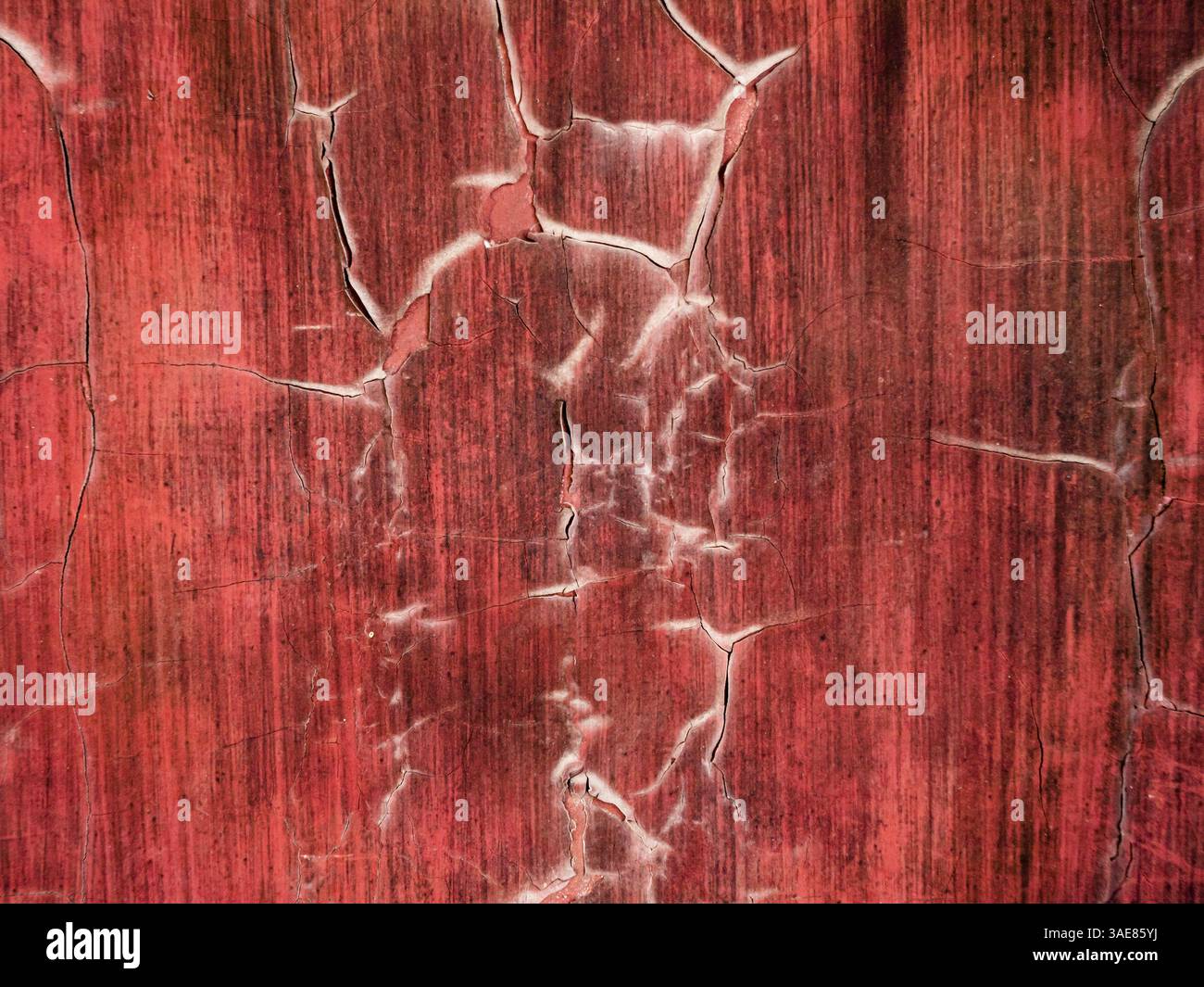 Gros plan détaillé de peinture rouge fissurée révélant des textures sur une vieille surface dans un environnement altéré Banque D'Images