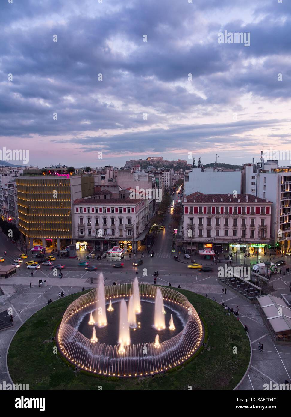 Athènes, Grèce - 5 avril 2025 : vue aérienne du centre-ville d'Athènes au crépuscule, avec une fontaine circulaire illuminée et des bâtiments historiques Banque D'Images