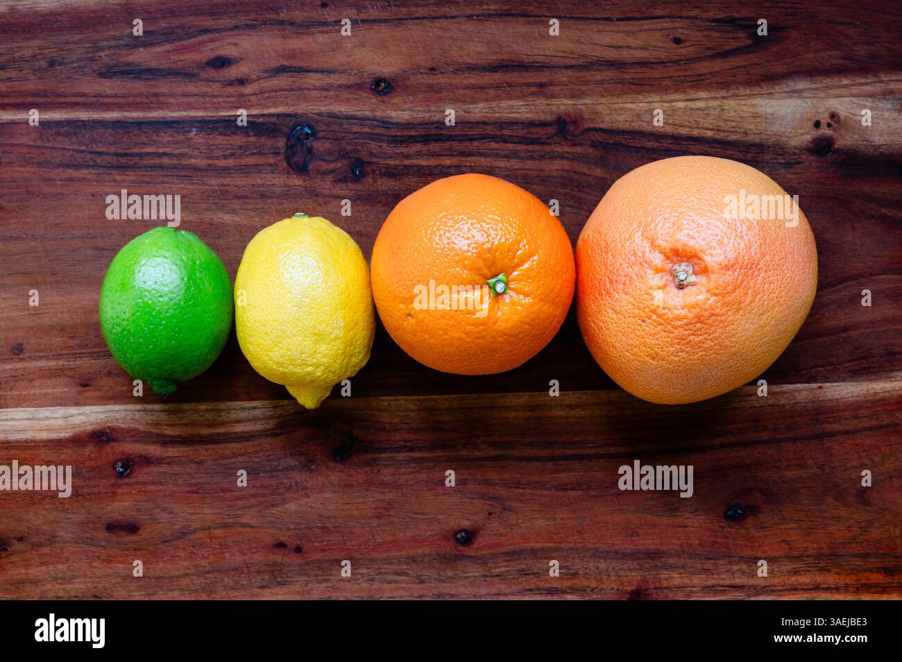 Citron vert, citron, orange et pamplemousse alignés sur une planche à découper en bois Banque D'Images