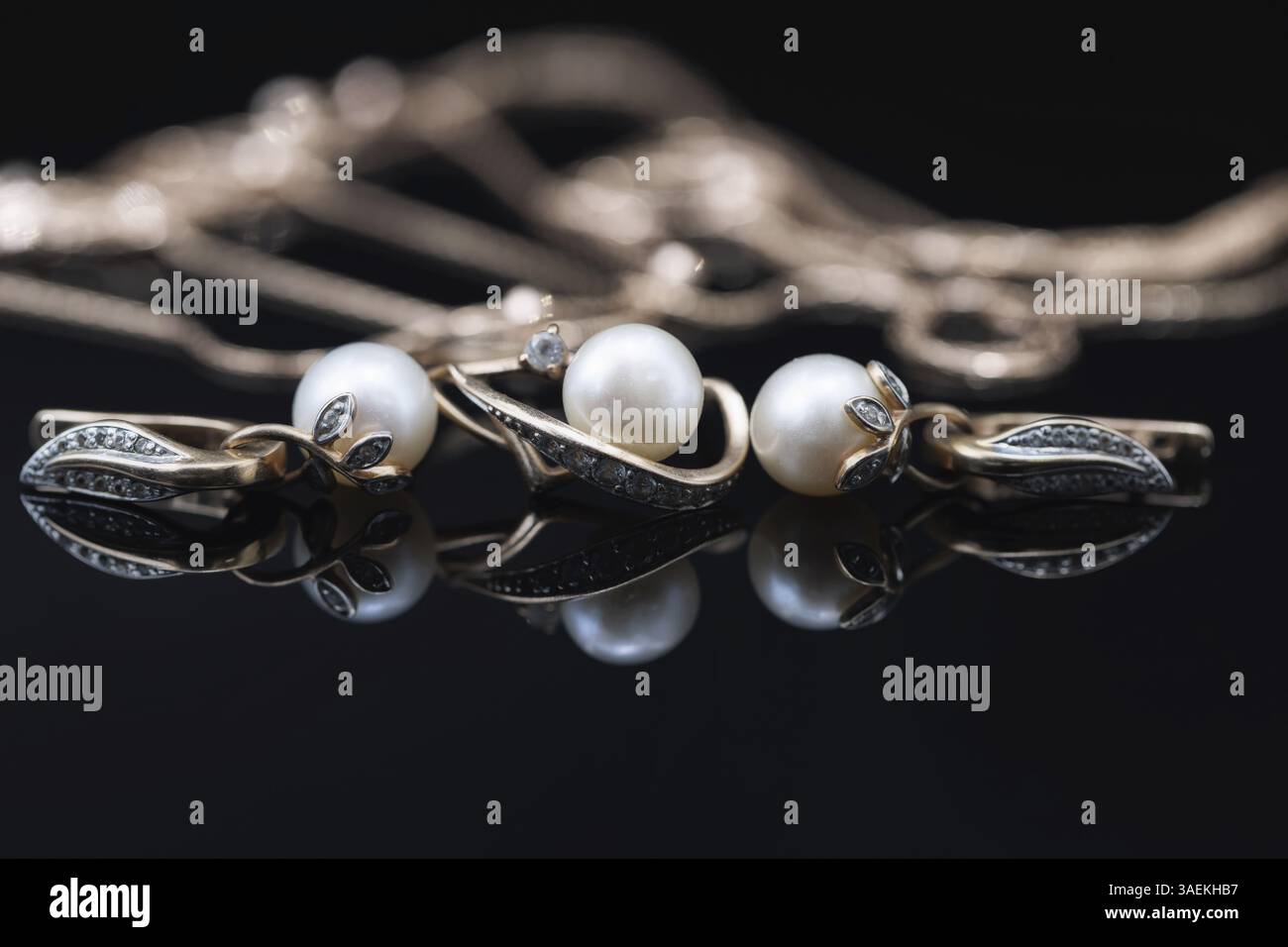 Les boucles d'oreilles et les bagues dorées ornées de perles blanches se trouvent sur une surface noire du miroir Banque D'Images