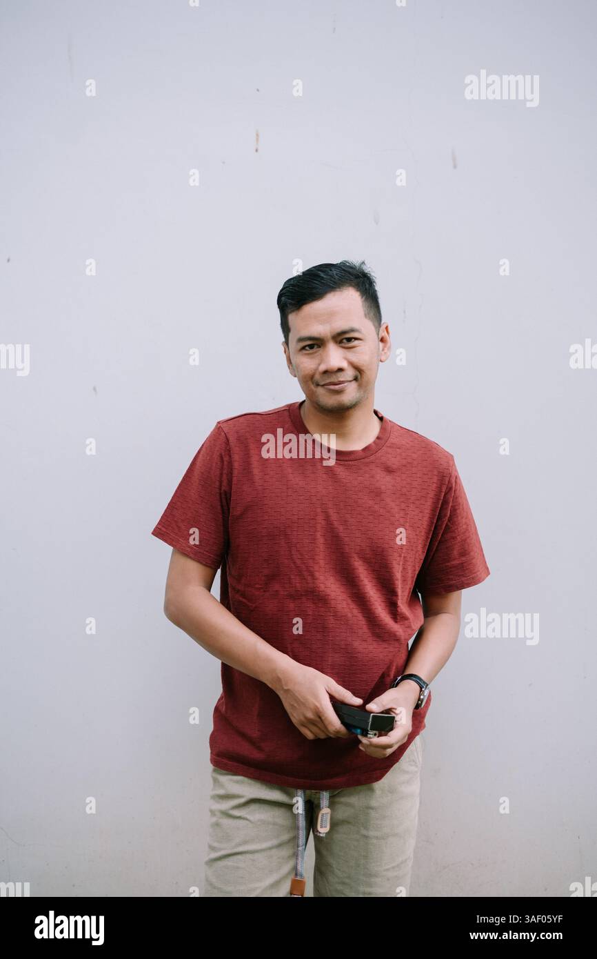 Homme asiatique souriant dans la chemise couleur brique posant devant le mur Uni. Portrait confiant et décontracté. Banque D'Images