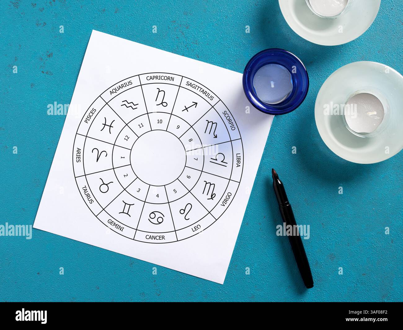 Carte natale imprimée avec des signes du zodiaque, des bougies et un stylo sur fond bleu, créant une atmosphère spirituelle pour l'astrologie et les lectures d'horoscope Banque D'Images