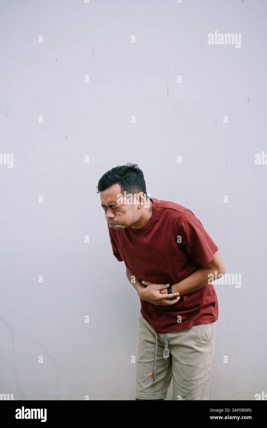 Homme souffrant de douleurs à l'estomac. Il tient son abdomen avec les deux mains avec une expression de douleur. Banque D'Images
