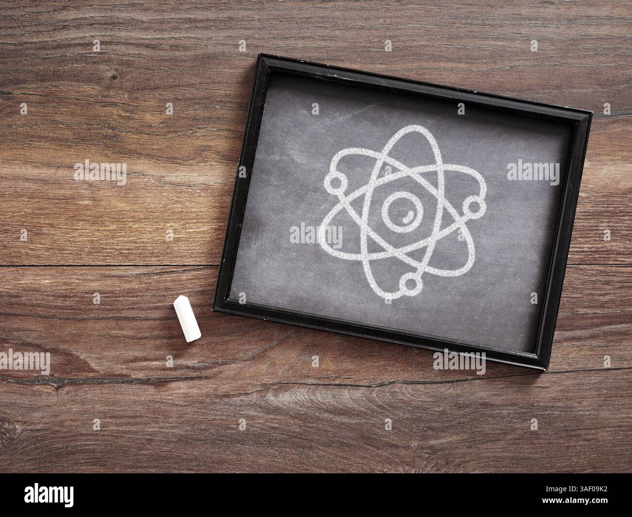 Atom Scheme est dessiné à l'aide de craie sur un petit tableau noir placé sur une table en bois avec un morceau de craie à côté. Concept d'enseignement des sciences. Banque D'Images