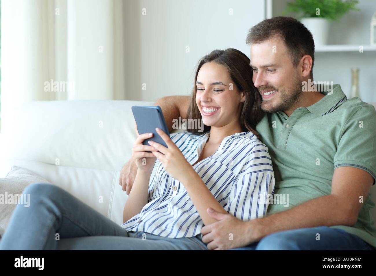 Heureux couple lisant ensemble un ebook assis sur un canapé à la maison Banque D'Images