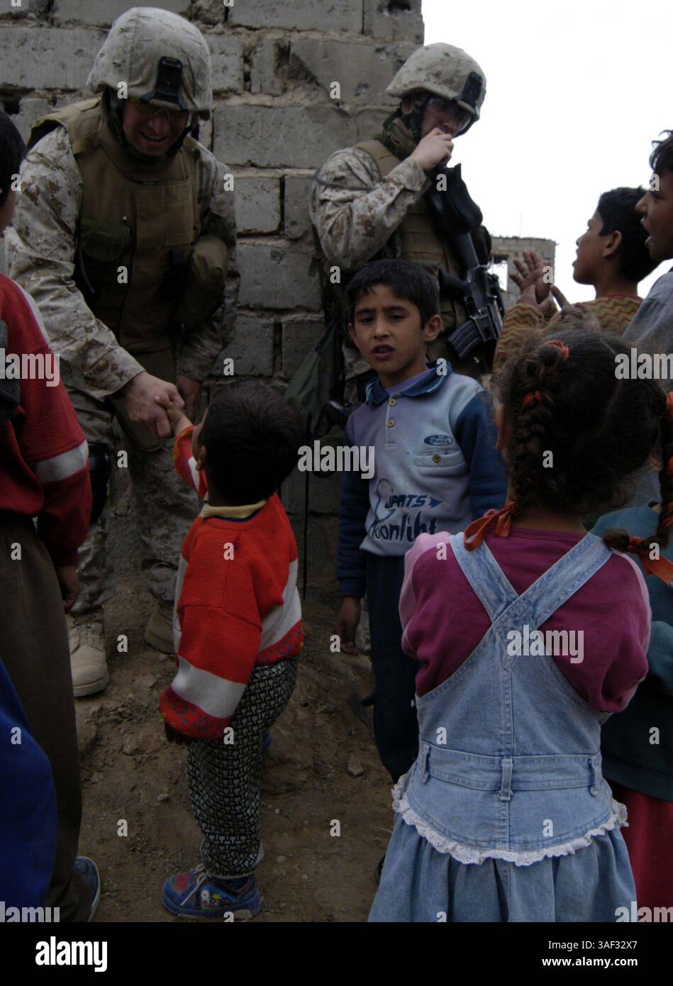 09 mars 2005 ; Fallujah, Irak ; Navy LTD.MATTHEW S. WEEMS, aumônier de 33 ans pour le 3e Bataillon, 4e Marines, Regimental combat Team-1, serre la main d'un garçon irakien en tant que second maître de 2e classe AARON G. NEELY, 21 ans spécialiste des programmes religieux pour le bataillon, assure la sécurité lors d'une patrouille dans la ville de Fallujah, Irak, le 9 mars. Weems et Neely participent à de nombreux aspects des opérations du bataillon pour maintenir une présence parmi les Marines. Banque D'Images