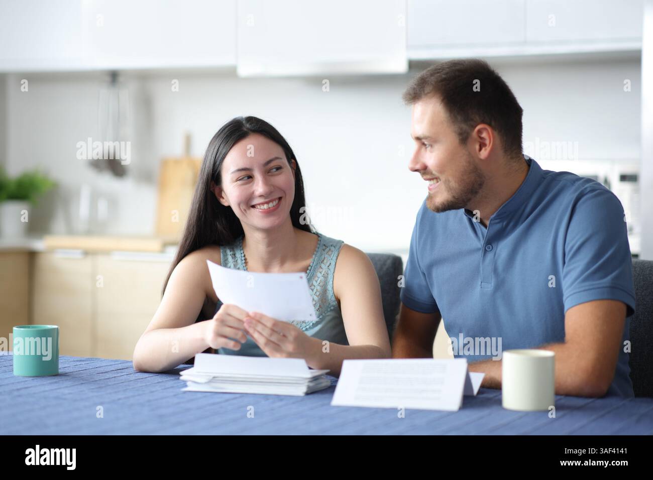 Heureux couple interracial parlant de relevé bancaire dans la cuisine à la maison Banque D'Images