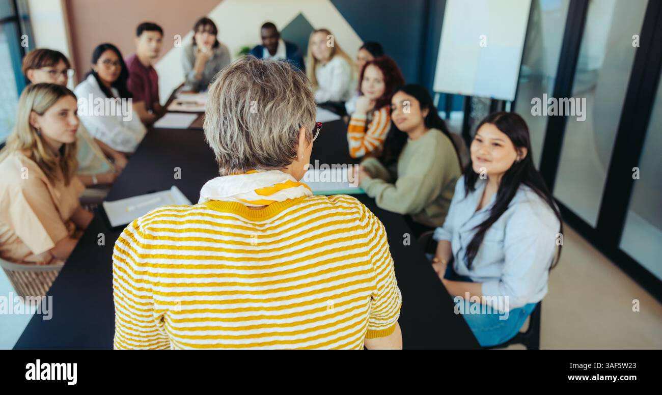 Un groupe diversifié de jeunes élèves écoute un enseignant pendant une séance en classe, favorisant l’engagement et l’apprentissage dans un environnement éducatif. Banque D'Images