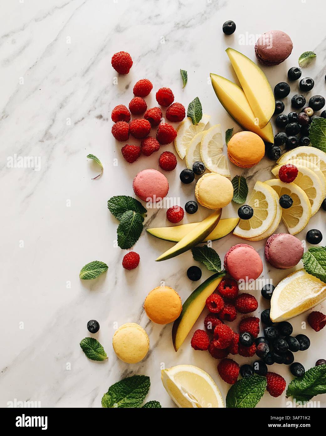 plan de dessus plat sur un fond de marbre. Motif de fruits, framboises, tranches de mangue, tranches de citron, bueberries, feuilles de menthe et rose, Banque D'Images