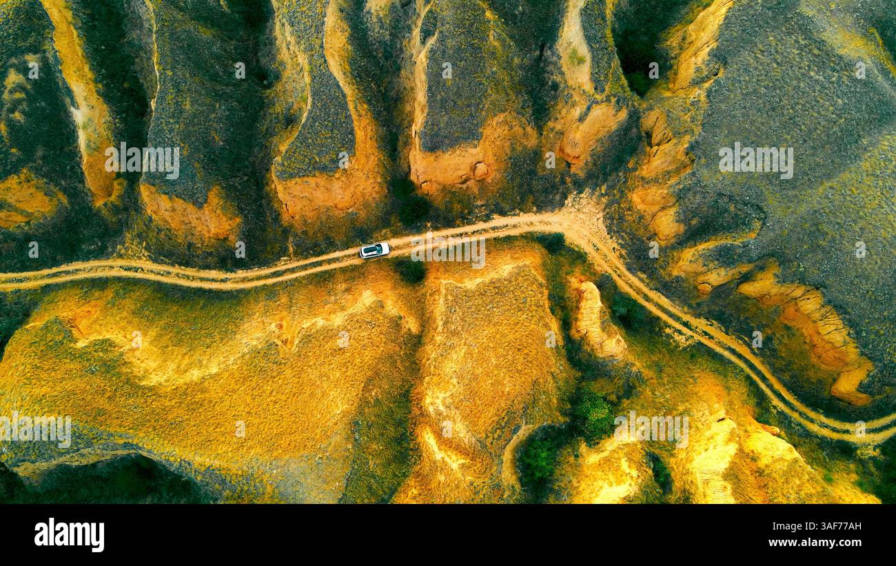 Vue aérienne d'une voiture sur un chemin de terre dans un paysage rocheux. Une vue aérienne saisissante d'une voiture blanche voyageant le long d'un chemin de terre serpentant à travers un rude Banque D'Images