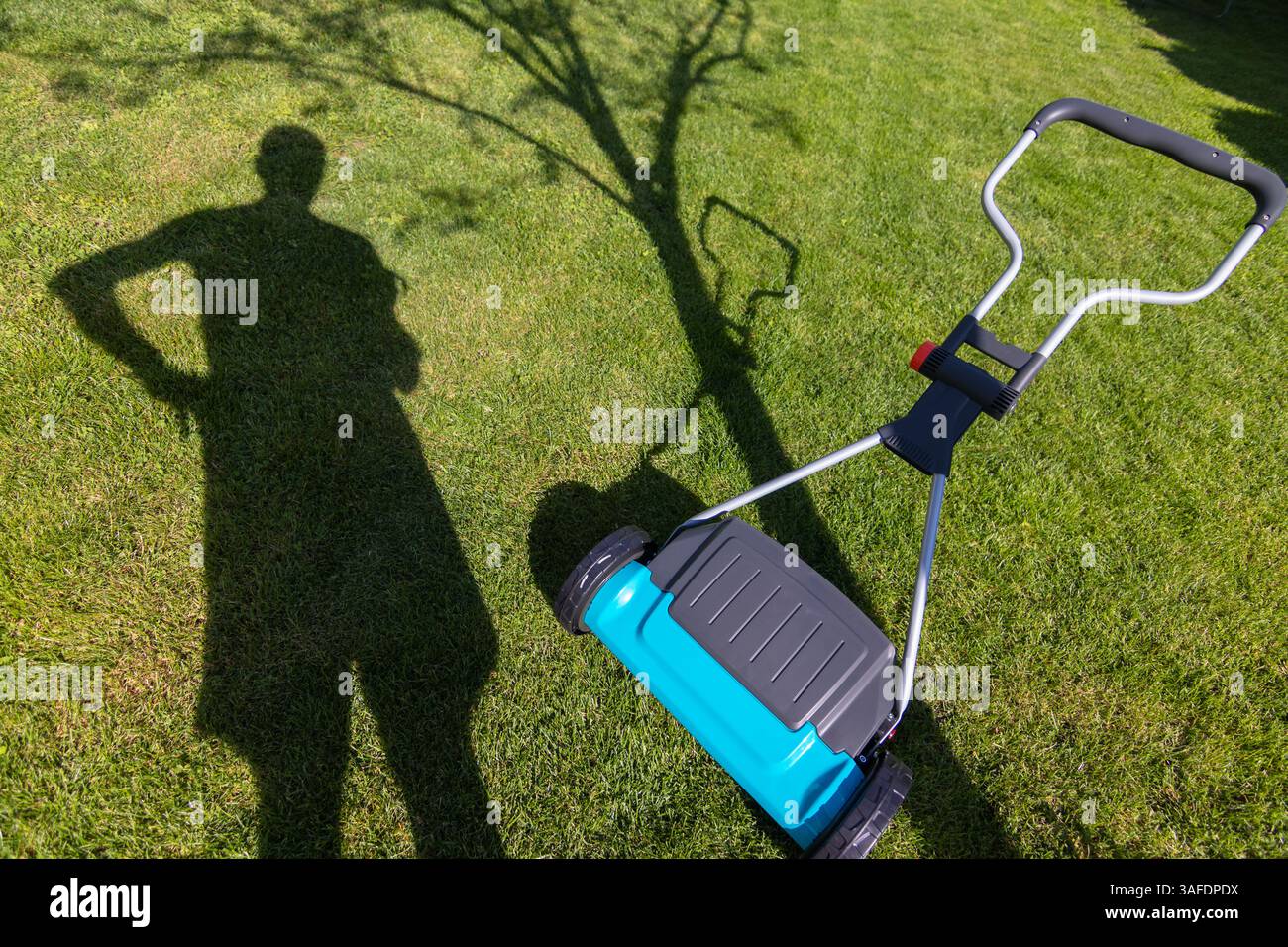 Ombre d'une personne debout près d'une tondeuse à gazon sur une pelouse verte pendant une journée ensoleillée, suggérant des soins de jardin et une activité de plein air. Banque D'Images