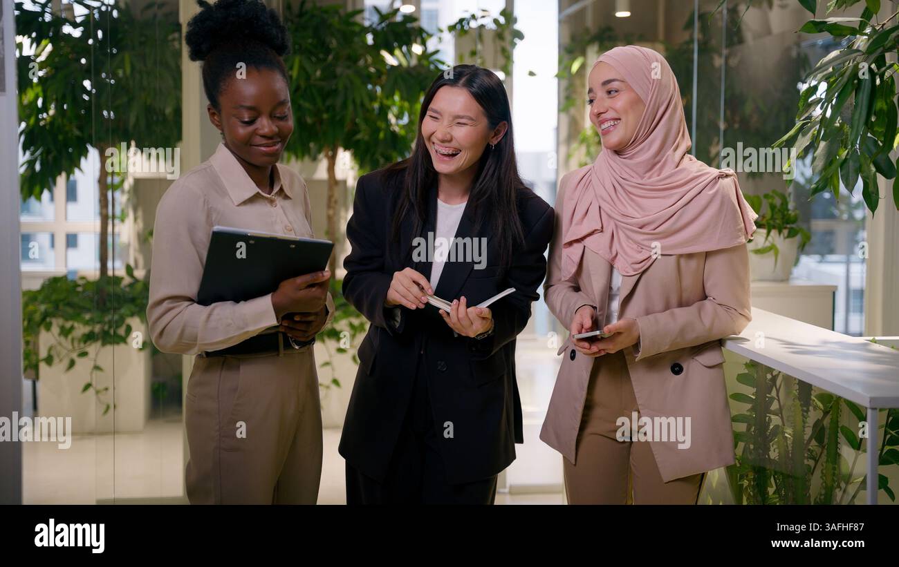 Divers collègues multiraciaux heureux partenaires d'affaires afro-asiatiques musulmanes femmes d'affaires souriantes filles riantes collègues dans le bureau bavardant parler Banque D'Images