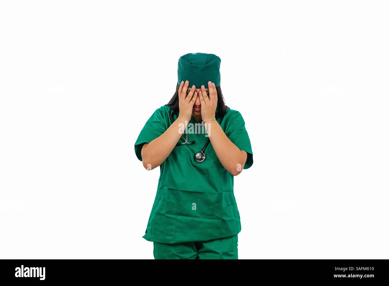 Jeune femme chirurgienne portant des gommages verts et stéthoscope couvrant son visage avec ses mains, exprimant la tristesse, la déception et le stress émotionnel o Banque D'Images