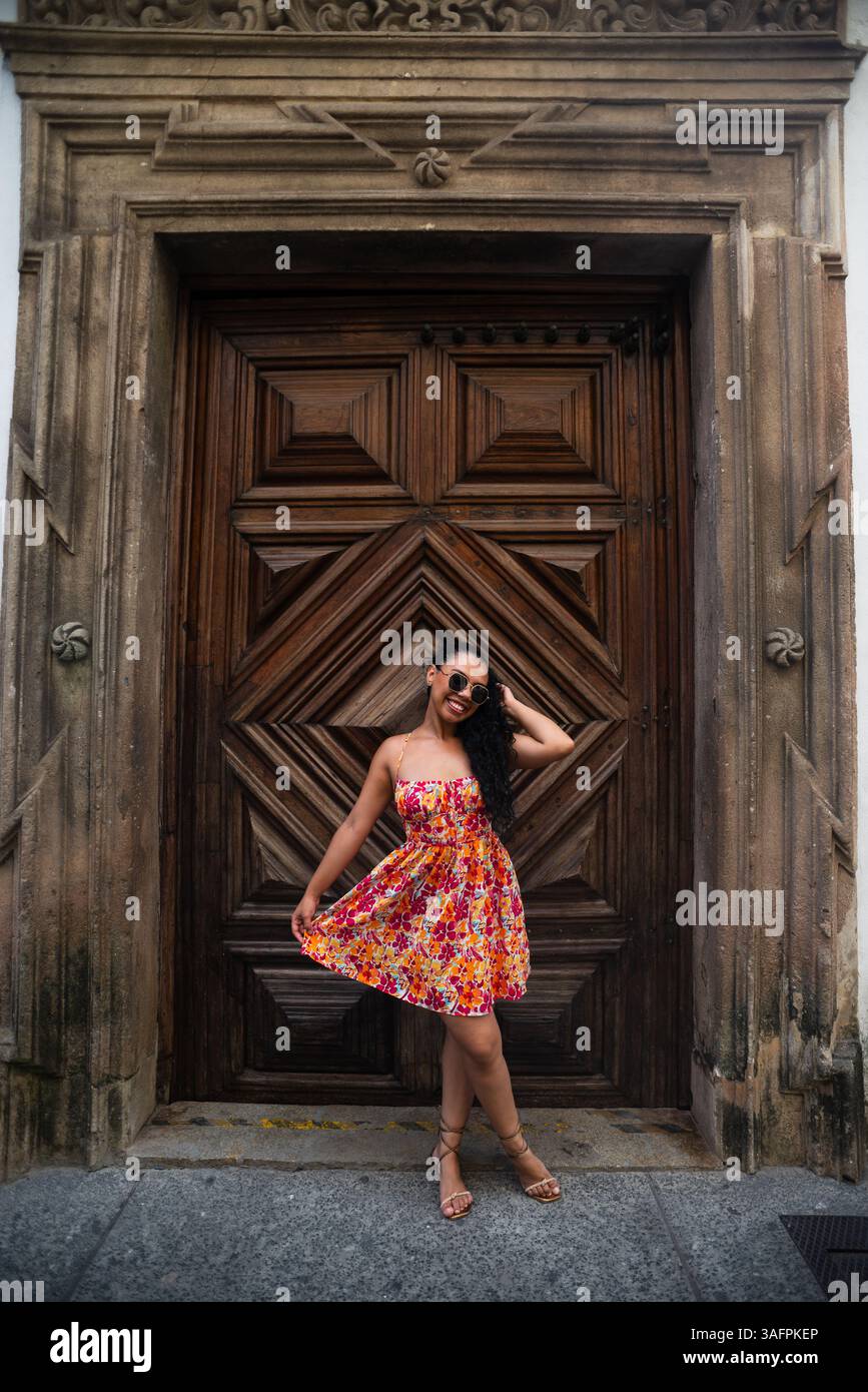 Jeune femme blanche avec des tresses et une robe colorée posant pour la caméra contre une grande vieille porte en bois. Personne voyageant. Brésil Banque D'Images
