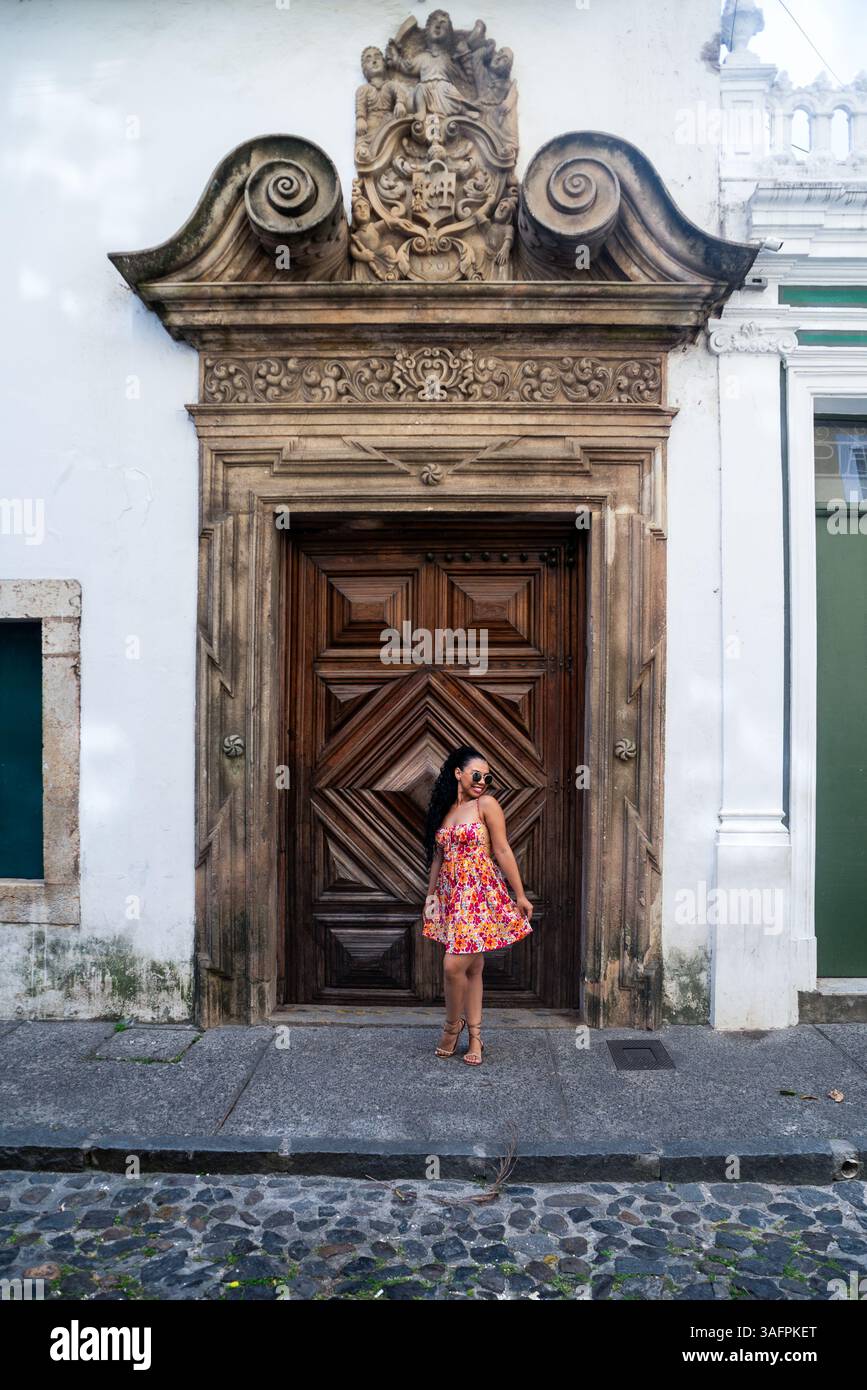 Jeune femme blanche avec des tresses et une robe colorée posant pour la caméra contre une grande vieille porte en bois. Personne voyageant. Brésil Banque D'Images