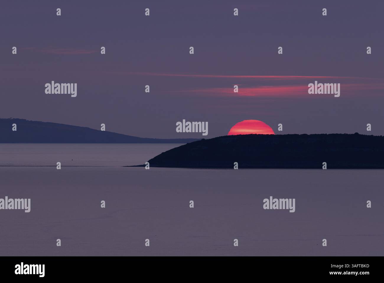Coucher de soleil, soleil coule rouge brillant dans un ciel violet derrière les îles d'Anglesey et Puffin Island dans la mer, Anglesey, pays de Galles, Grande-Bretagne Banque D'Images