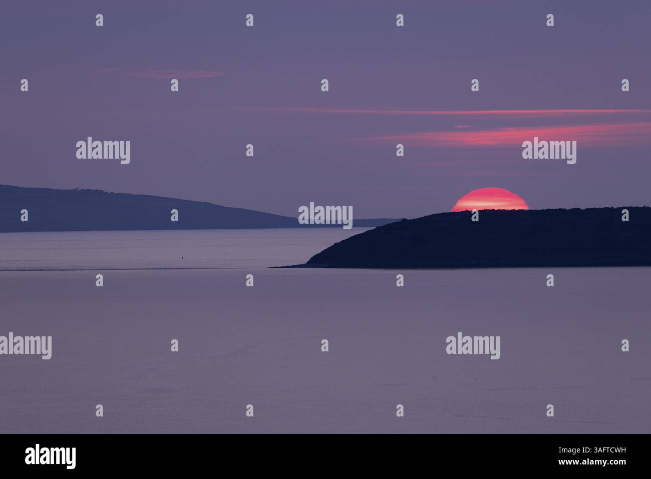 Coucher de soleil, soleil coule rouge brillant dans un ciel violet derrière les îles d'Anglesey et Puffin Island dans la mer, Anglesey, pays de Galles, Grande-Bretagne Banque D'Images
