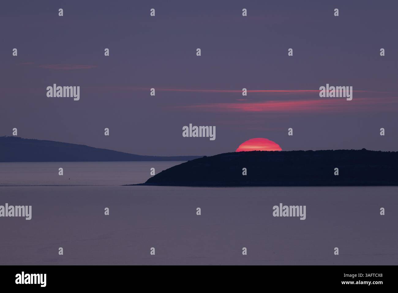 Coucher de soleil, soleil coule rouge brillant dans un ciel violet derrière les îles d'Anglesey et Puffin Island dans la mer, Anglesey, pays de Galles, Grande-Bretagne Banque D'Images