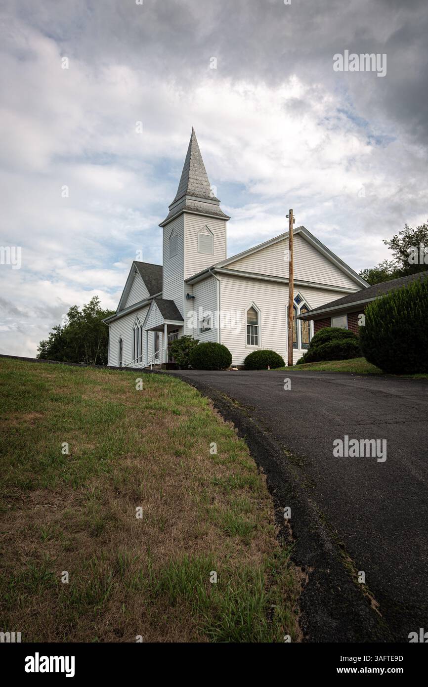 Église blanche au sommet d'une colline avec un ciel bleu et des nuages brisés derrière elle Banque D'Images