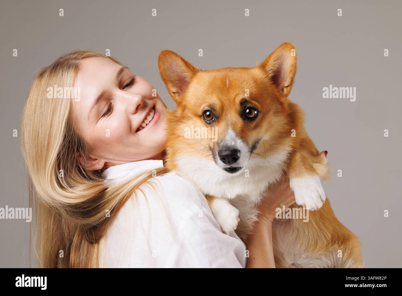 Jeune femme joyeuse tenant son adorable chien Corgi, à la fois heureux et affectueux, dans un moment rapproché. Banque D'Images