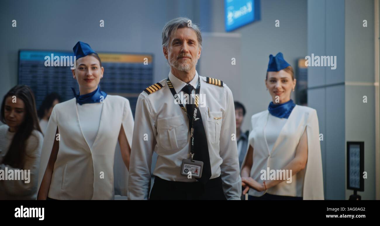 Portrait de pilote de ligne professionnel et deux beaux agents de bord dans des uniformes élégants souriant, regardant la caméra. Membres d'équipage de conduite dans le terminal de l'aéroport international bondé. Prise de vue moyenne. Banque D'Images