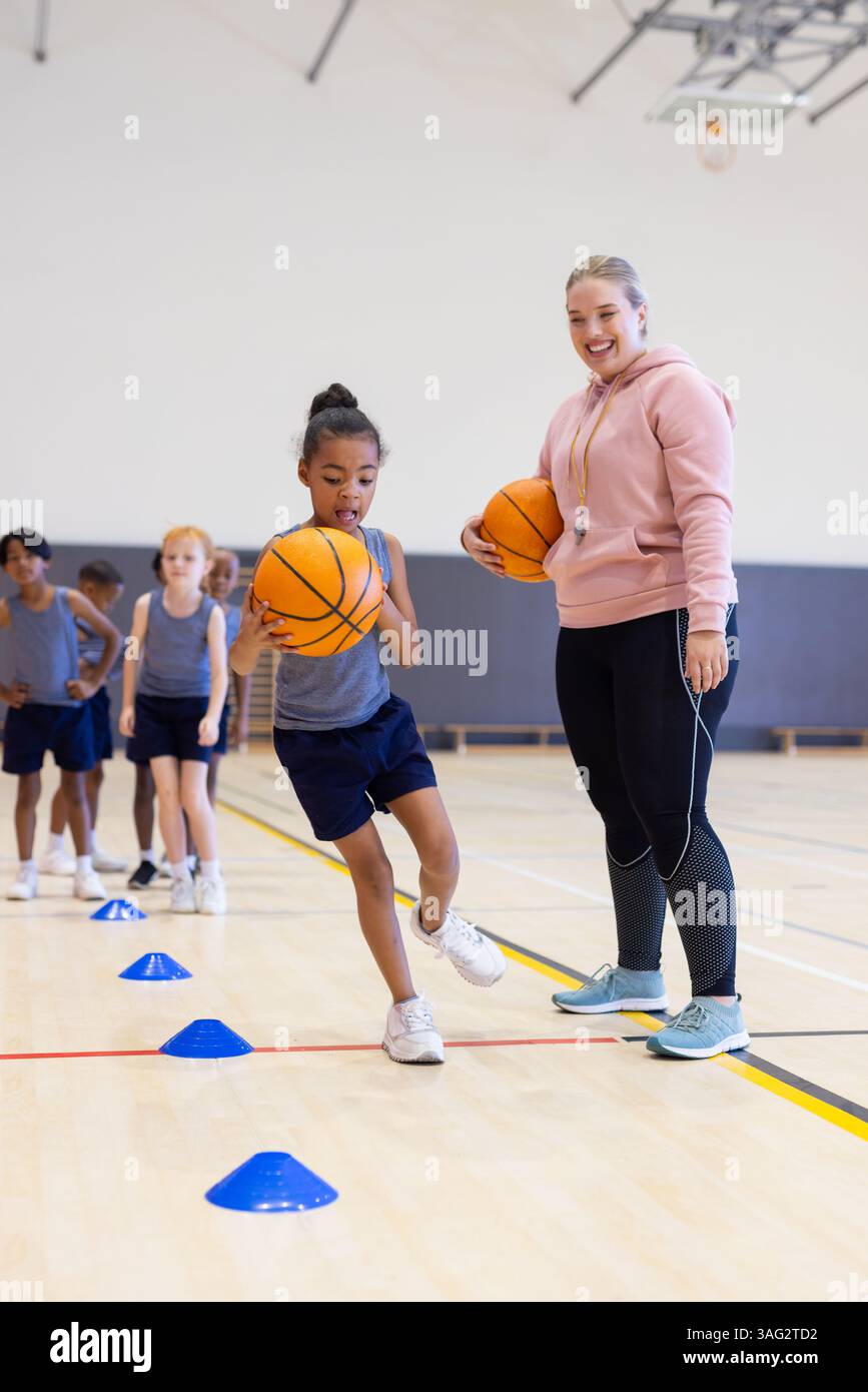 Jouer au basket-ball, balle dribble fille dans le gymnase de l'école avec entraîneur féminin souriant Banque D'Images