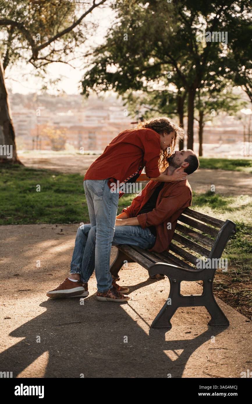 Moment romantique capturé dans un parc comme un couple partage une étreinte intime sur un banc. L'homme est assis tandis que la femme se penche sur, créant une tendresse et l Banque D'Images