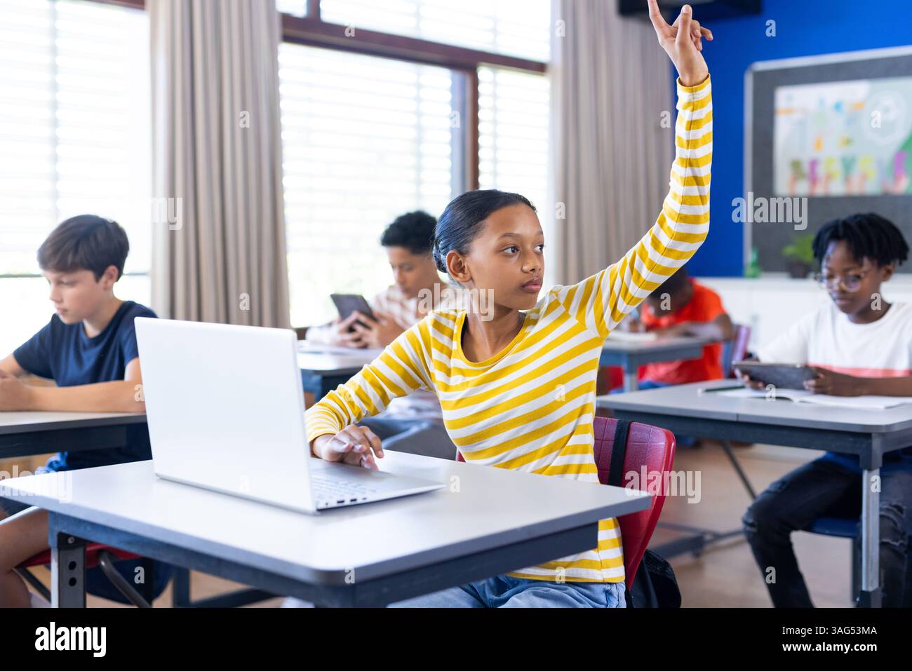 À l'école, fille levant la main tout en utilisant un ordinateur portable en classe Banque D'Images