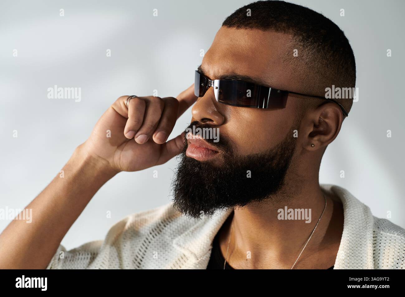 Un jeune homme élégant pose soigneusement dans des lunettes de soleil à la mode, exsudant le charisme dans un espace élégant. Banque D'Images