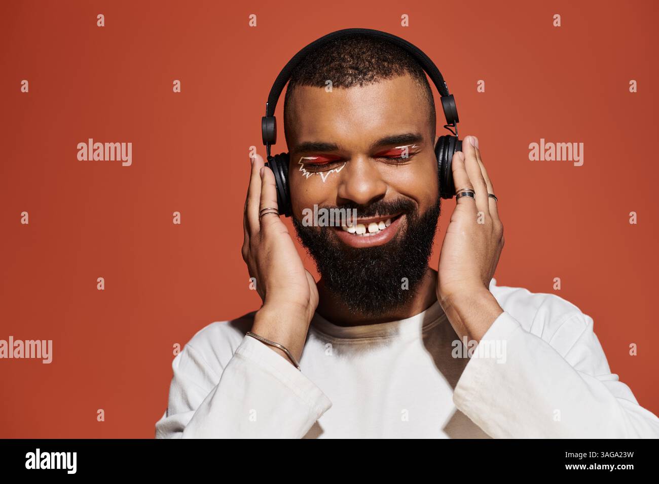 Jeune homme avec un look à la mode sourit tout en portant des écouteurs, immergé dans les vibrations de la musique. Banque D'Images