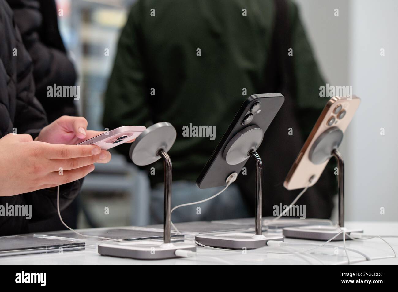 Vitrine avec smartphones dans le magasin d'électronique. Nouveaux iPhones Apple en magasin. Mains du client, choisir un smartphone. Minsk, Biélorussie - 16 mars 2025 Banque D'Images