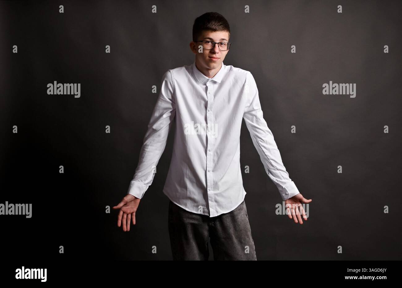 le jeune homme sur le fond gris étend ses bras, paumes vers le haut. Banque D'Images