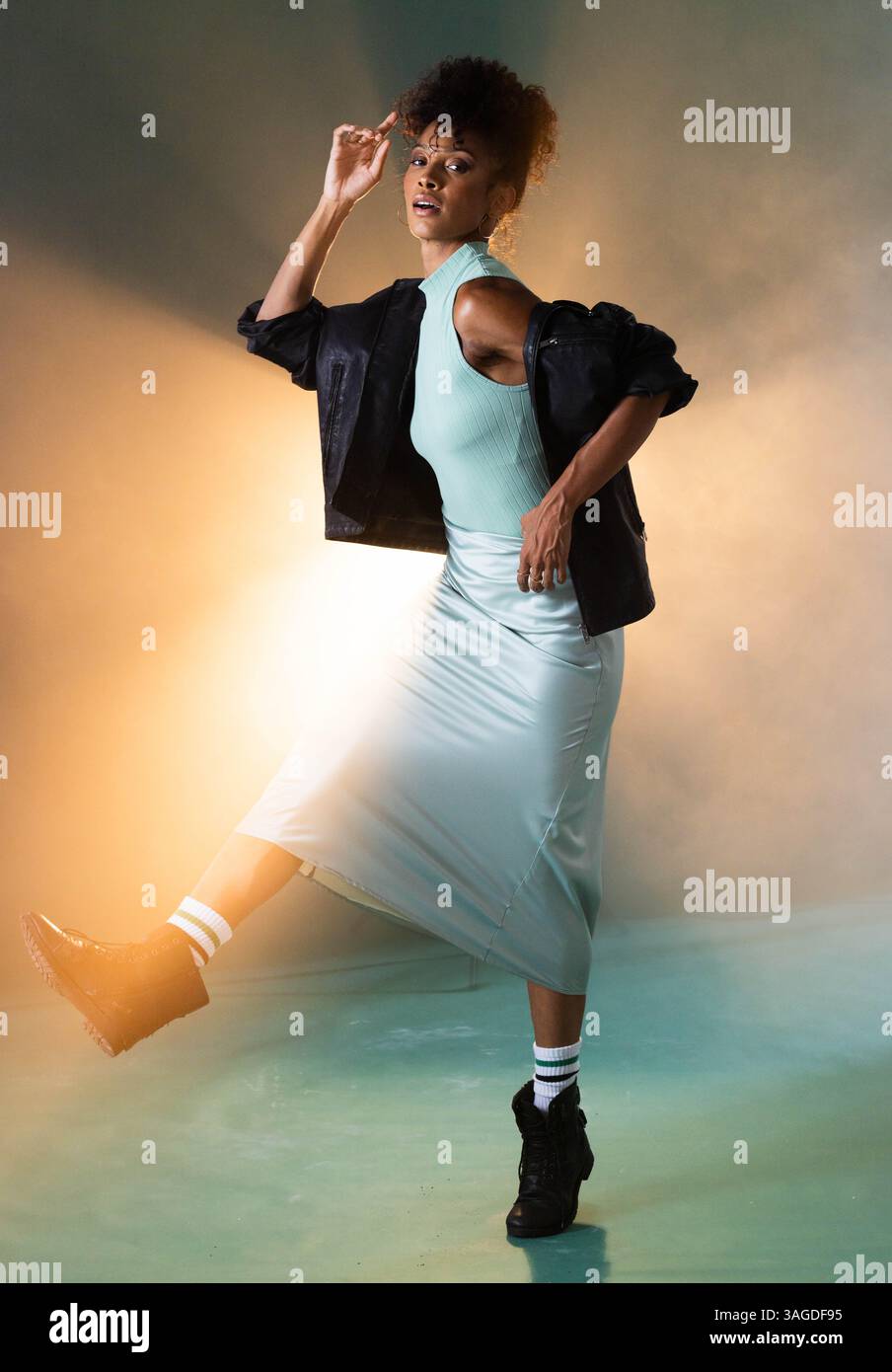 Femme à la mode dans une tenue élégante dansant énergiquement dans un éclairage de studio vibrant. style, danse, coloré, expression, tendance, mouvement Banque D'Images