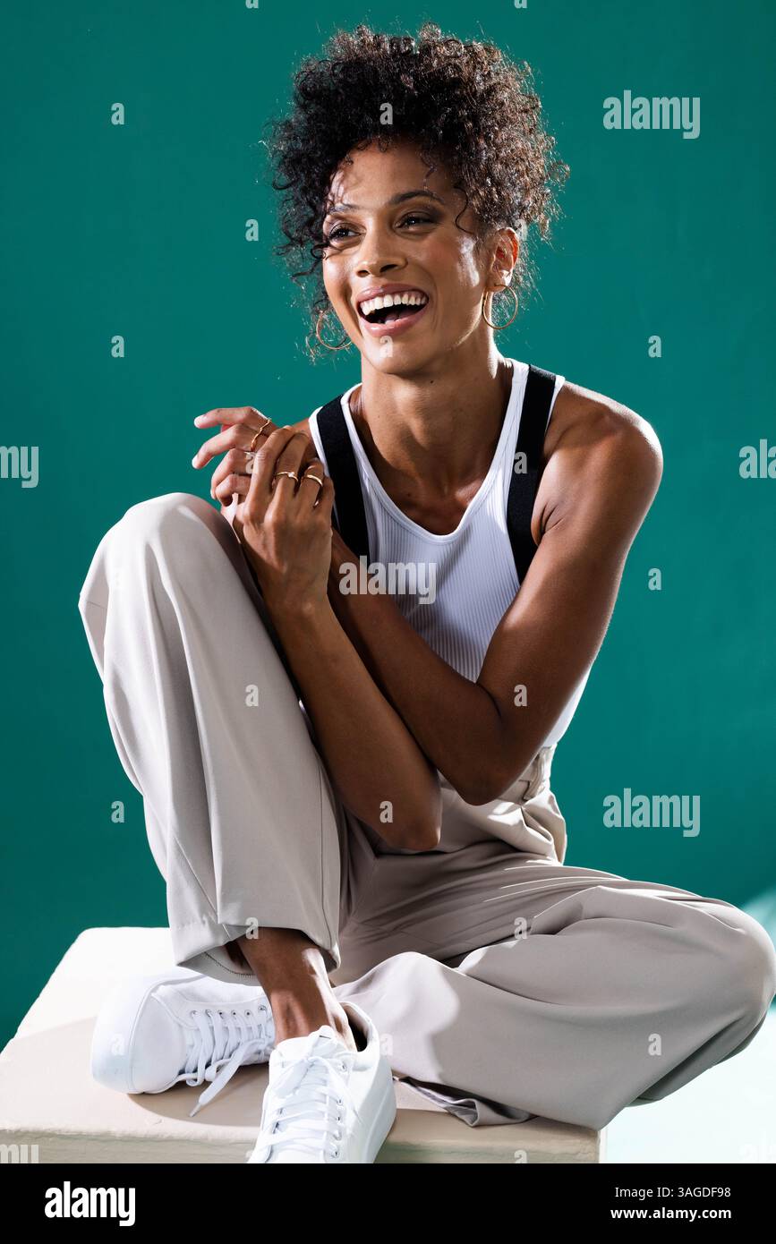 Femme souriante dans une tenue décontractée assise sur un tabouret, profitant d'un moment détendu. Détente, style de vie, bonheur, loisirs, mode, paisible Banque D'Images