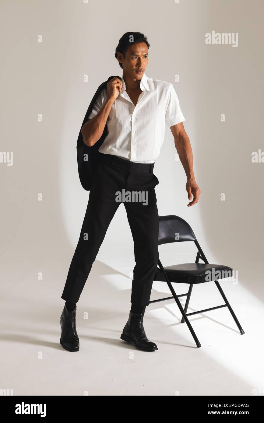 Homme confiant dans une tenue élégante posant avec veste dans un studio moderne. Mode, style, portrait, confiance, vêtements pour hommes, tendance Banque D'Images