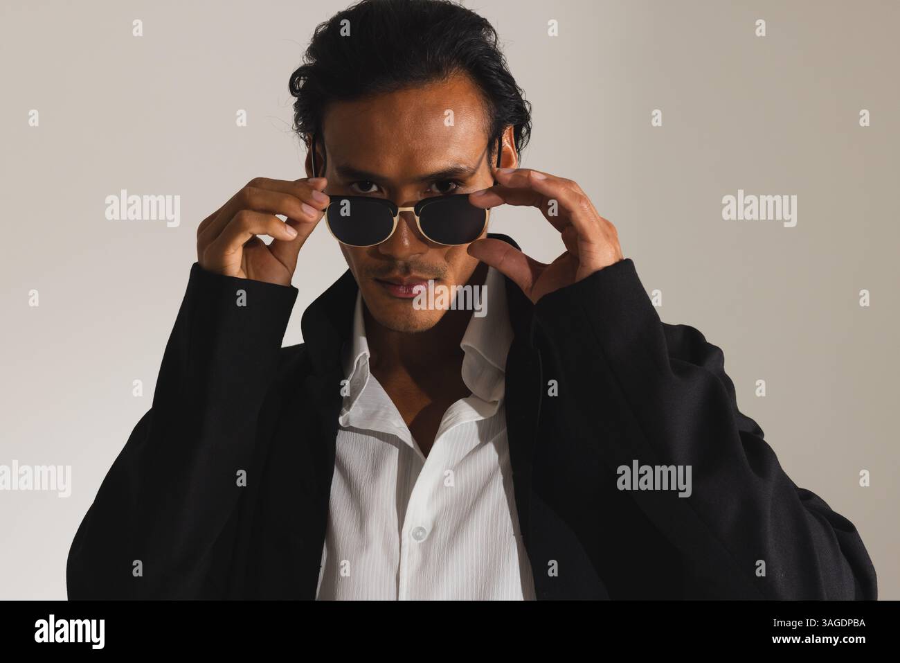 Homme confiant ajustant les lunettes de soleil portant un manteau noir élégant dans le studio de mode. style, confiance, vêtements, homme, tendance, gras Banque D'Images
