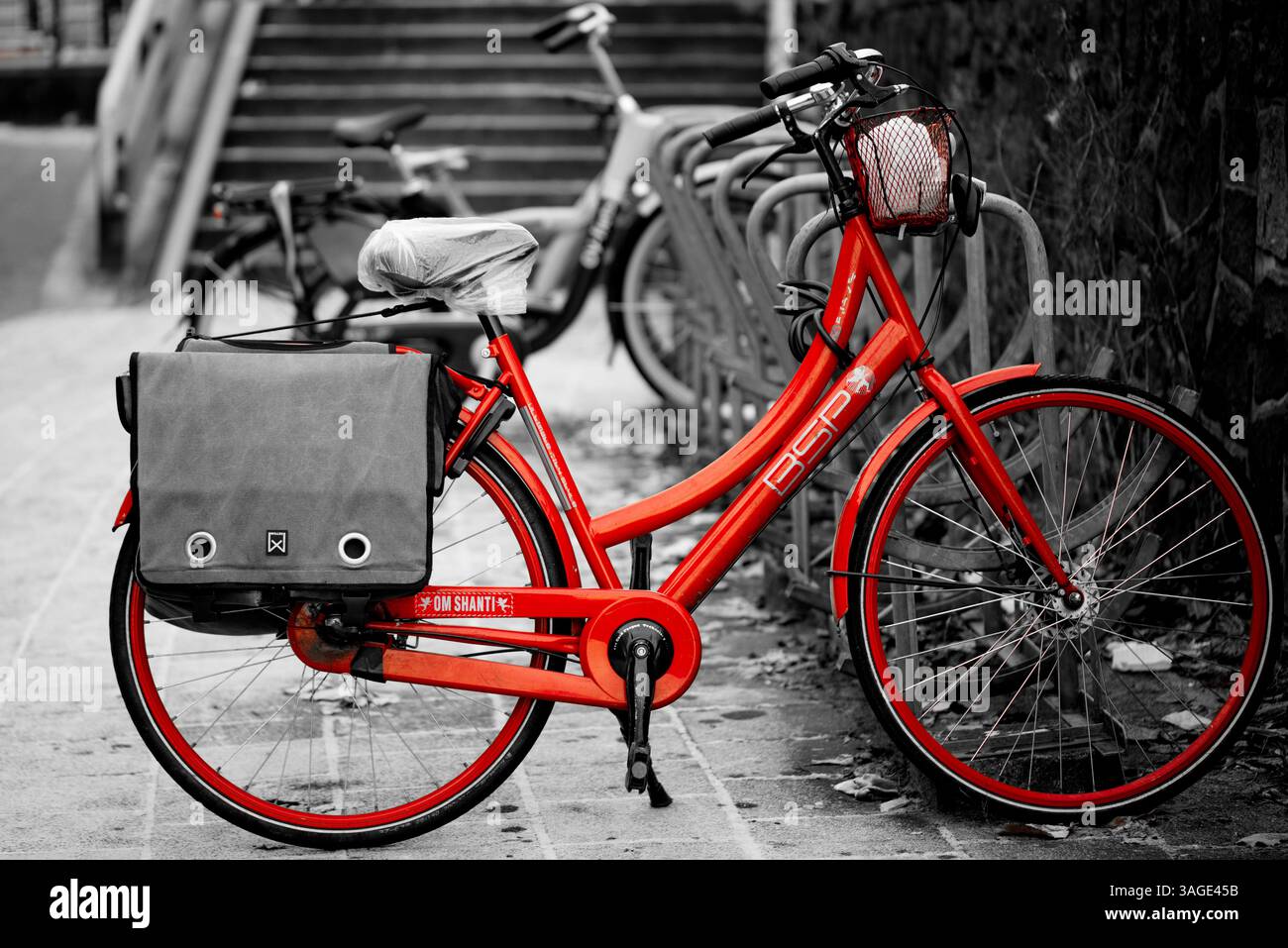 Un vélo BSP rouge vif avec texte « Om SHANTI », garé dans un porte-vélos à Amsterdam, aux pays-Bas, créant un contraste visuel audacieux avec son environnement Banque D'Images